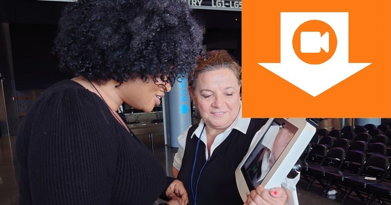 Two women watching the video that was self-recorded using StoryBooth Kiosk; in the background is a convention center.